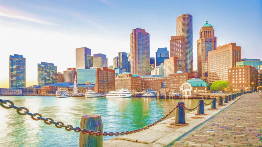 Boston skyline at sunset, showcasing the harbor with vibrant colors reflecting on the water.