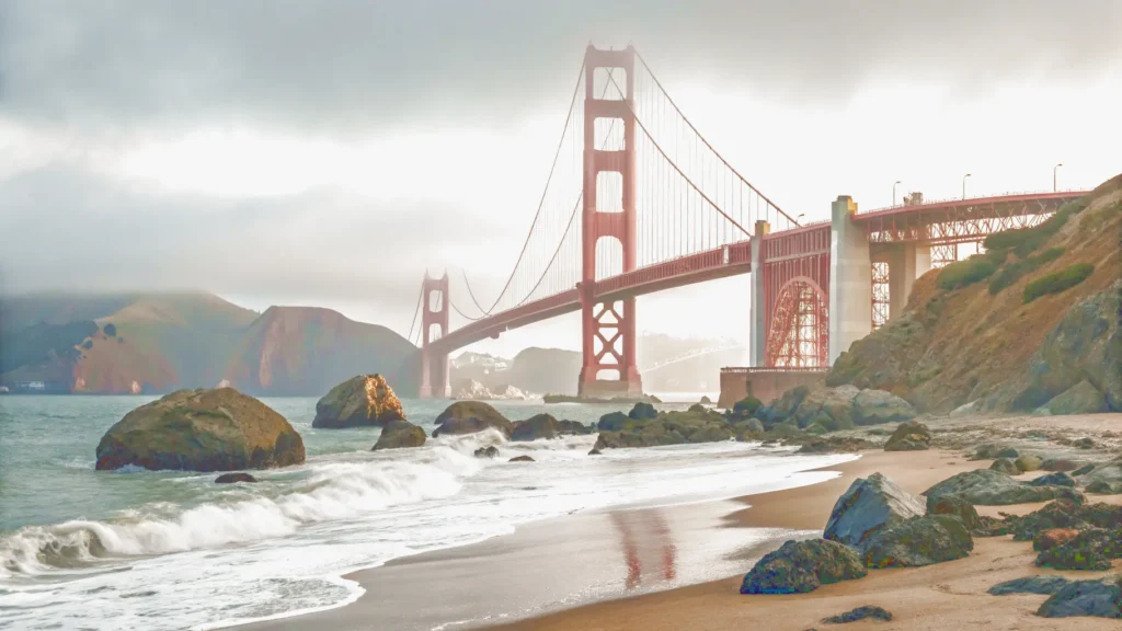 The Golden Gate Bridge viewed from a rocky beach at sunset with fog rolling in, a key stop on a west coast road trip.