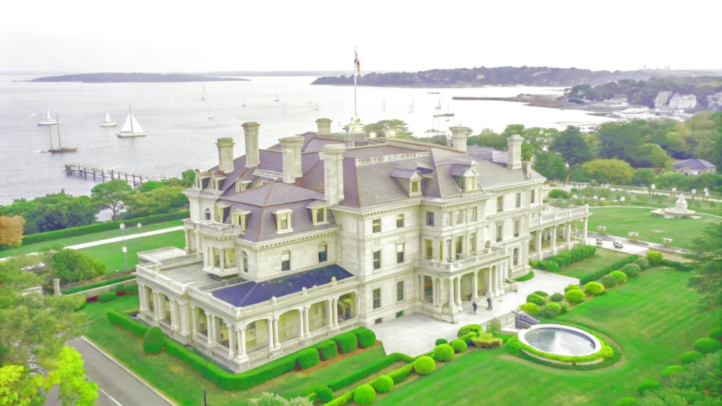 . Overhead shot of an expansive mansion with manicured lawns and a serene water feature, highlighting a New England road trip.